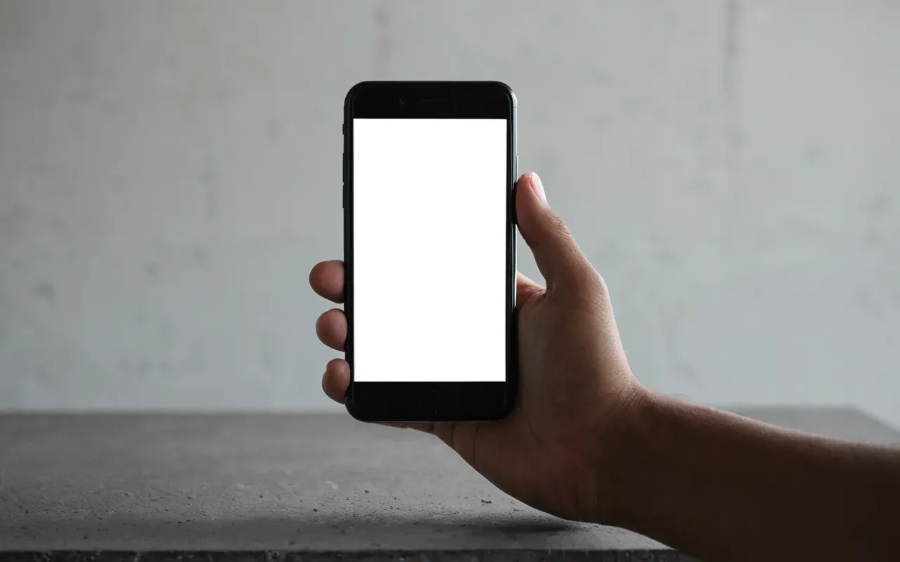 mobile device interaction Close-up of a hand holding a modern smartphone with a blank white screen standing on a concrete table surface in soft diffused studio lighting